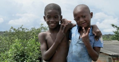Two young boys with their arms around each other, one makes a peace sign with his fingers