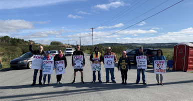 Group of people standing across a road holding picket signs