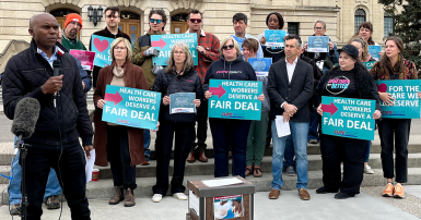 Person holding a microphone in front of  group holding placards 