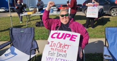 Woman sitting on a lawn chair holding a picket sign and raising a fist