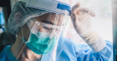 Nurse wearing plastic face shield leaning their head ahainst their hand 