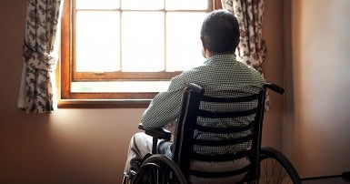 Homme âgé en fauteuil roulant regarde par la fenêtre