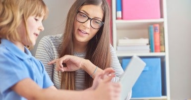 An education support worker sits at a table with a child holding a tablet