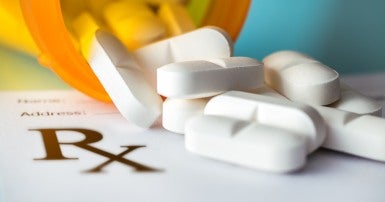 Image of white pills spilling out of an orange pill bottle onto a prescription pad