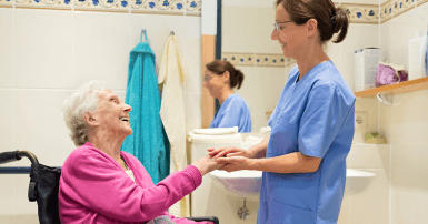 Long term care worker holding hand of elderly woman in wheelchair