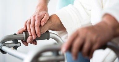 Close up on an elderly woman's hand on the handle of a walker, with a younger woman's hand resting on it gently