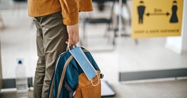 A person holding a backpack and a paper mask from the legs down.