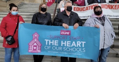 PEople standing on the steps of a building holding a banner in support of education workers