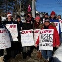 Group of men and women in winter clothing, wearing CUPE strike signs with slogans