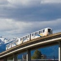 Image of Vancouver SkyTrain, elevated light rapid transit train and track with mountains and blue sky in the background.