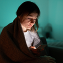 Person wrapped in blanket in a dark room looking at their phone