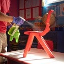 Man in red shirt  and blue gloves sprays cleaner on red children's chair