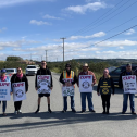 Group of people standing across a road holding picket signs