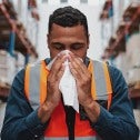 Young Black warehouse worker blowing his nose
