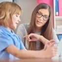 An education support worker sits at a table with a child holding a tablet