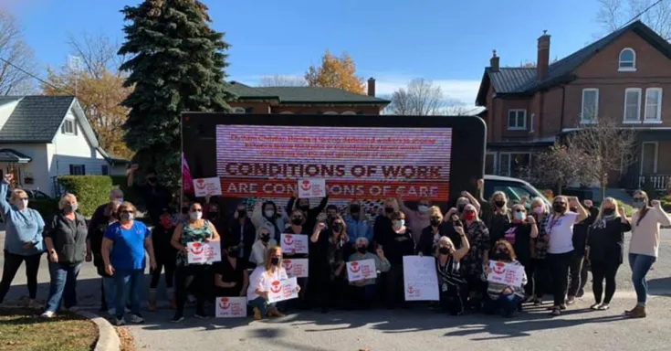 Group of workers wearing masks and holding signs that say "Conditions of work are conditions of care"