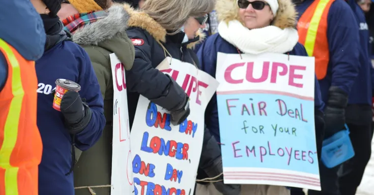 Crowd of women in winter coats and carrying CUPE strike signs