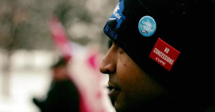 A man in profile wearing a black tuque with a red button that says NO CONCESSIONS