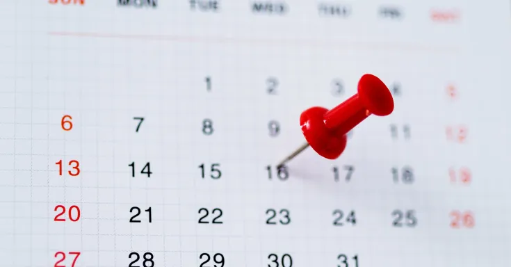 Blurred calendar page with red pushpin on 16