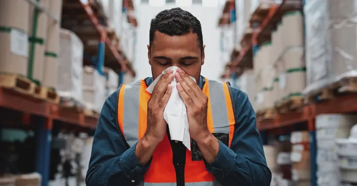Young Black warehouse worker blowing his nose