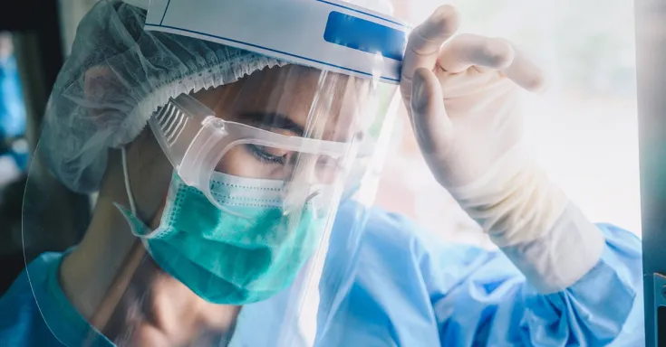 Tired healthcare worker wearing scrubs, a mask, goggles, and shield 