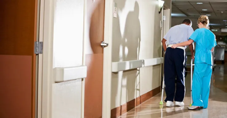 Woman in scrubs assisting an elderly man with a walker 