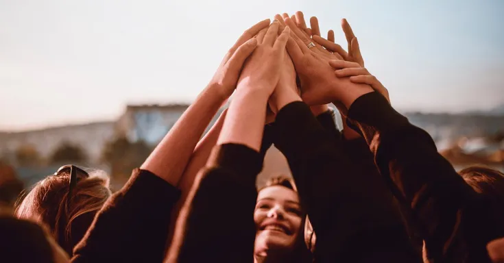 Soft focus image of a small group of women with their arms raised, touching hands