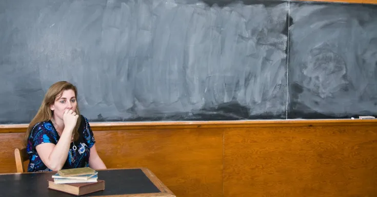 Worried female teacher at desk in front of blank blackboard