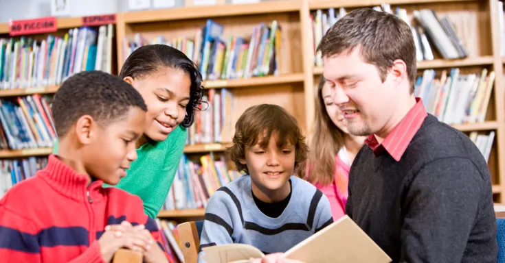Man reading a book to four children with bookshelves in the background
