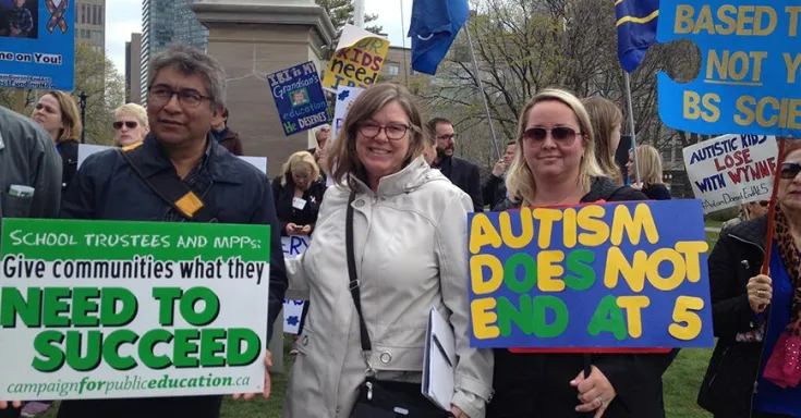 Two women and one man hold autism activism signs at a protest