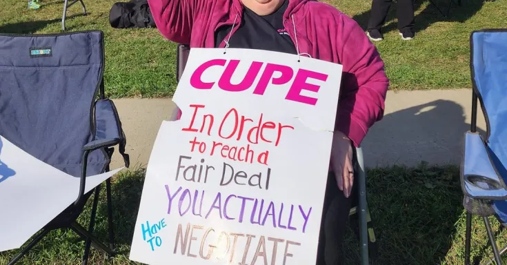 Woman sitting on a lawn chair holding a picket sign and raising a fist