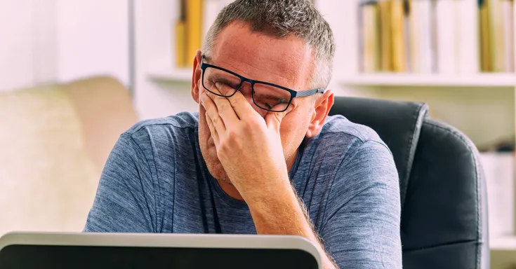 Close up of man with short salt and pepper hair and glasses, rubbing his eyes