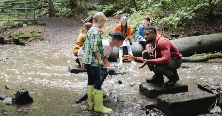 Students listen to instructor by a water stream in a forest