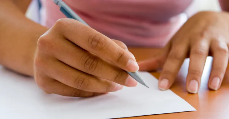 Hands holding a pencil poised above a piece of white paper