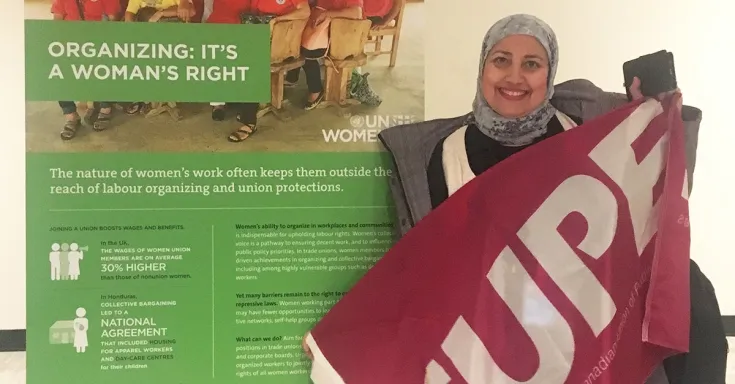 A woman holding a bright pink CUPE flag standing beside poster that includes the text "Organizing: It's a woman's right"