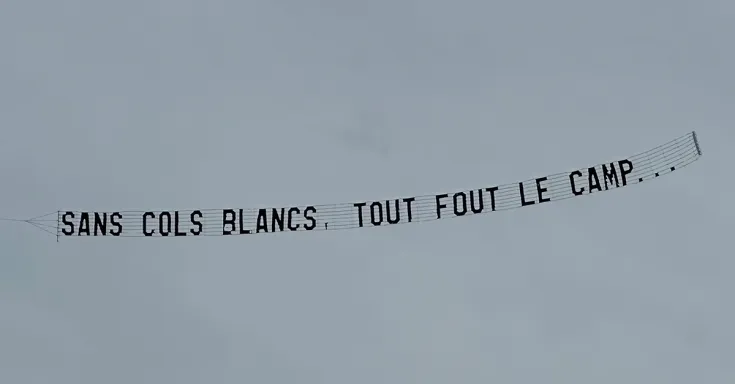Plane flying a banner that reads sans cols blancs, tout fout le camp