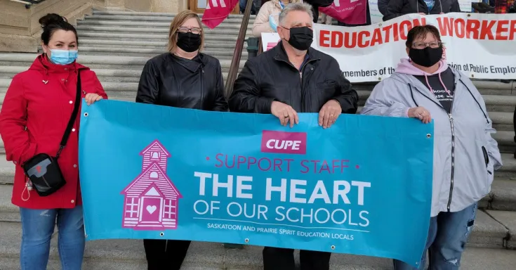 PEople standing on the steps of a building holding a banner in support of education workers